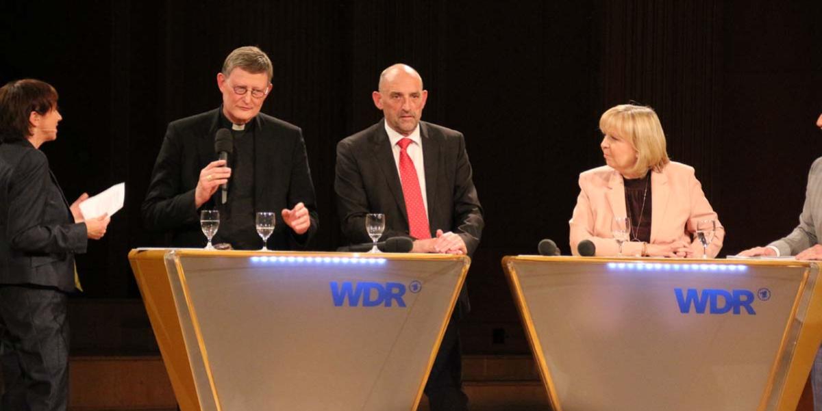 Kardinal Woelki im Podiumsgespräch. Die Ministerpräsidentin und Detlef Scheele hören ihm gespannt zu.