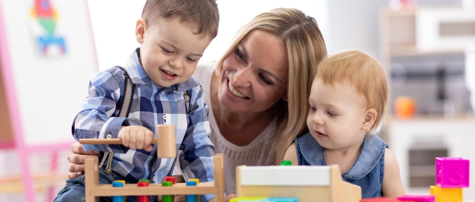 Kinderbetreuerin mit zwei Kleinkindern mit Holzspielzeug am Tisch