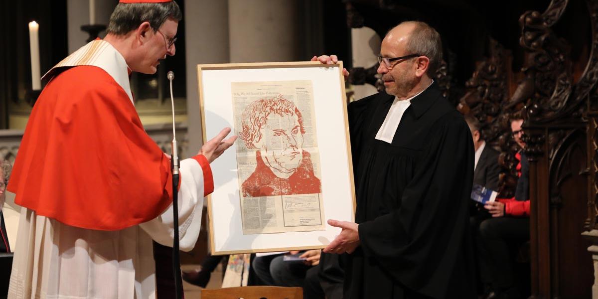 Kardinal Woelki überreicht Präses Rekowski ein besonderes Gastgeschenk: Einen Kunstdruck von Martin Luther auf einer Ausgabe der New York Times aus einer limitierten Auflage eines österreichischen Künstlers.