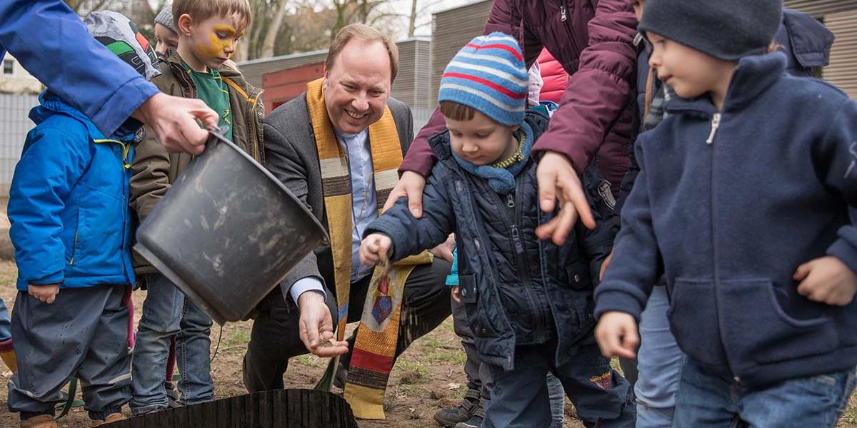 Stadtdechant Monsignore Robert Kleine streut zusammen mit den Kindern der Kita St. Agnes das Saatgut aus