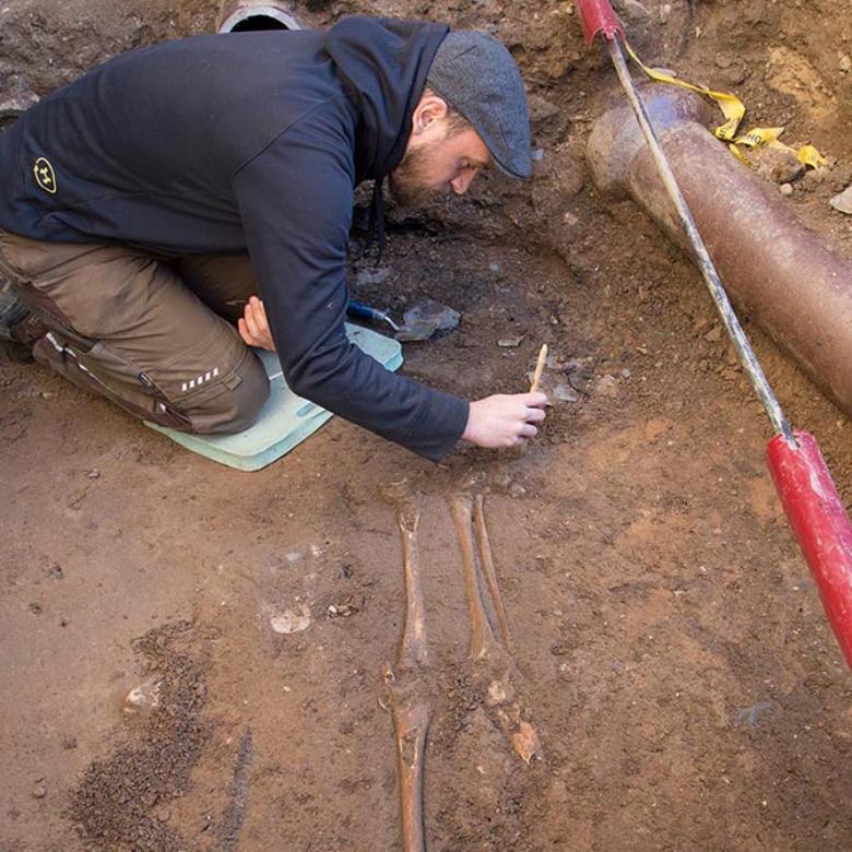 Im Kreuzgang wurden alte Gräber freigelegt. Ein Archäologe arbeitet mit einem Pinsel an den fragilen Stellen eines Skeletts.