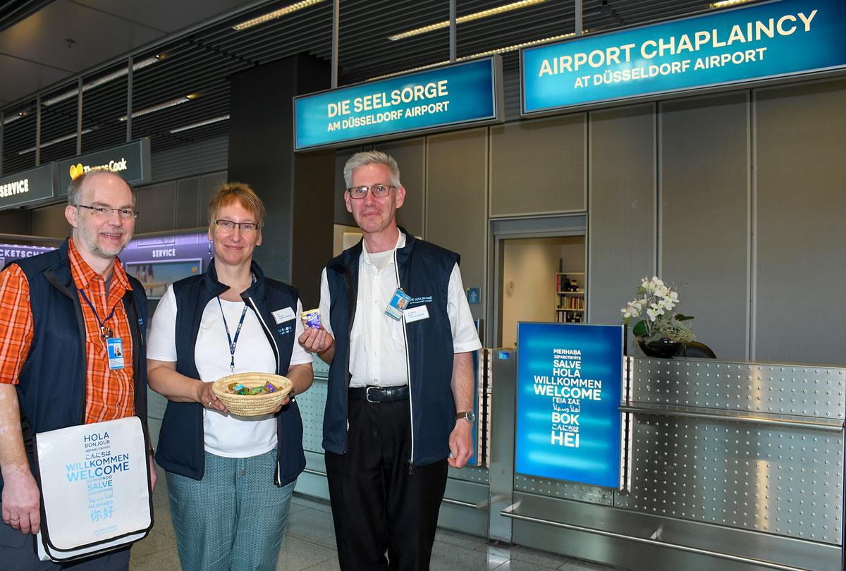 Der Schalter der Flughafenseelsorge in Terminal A, Abflugebene ist gut erkennbar an dem himmelblauen Logo.. Auf dem Bild (v.l.n.r.) sind Pastoralreferent Johannes Westerdick, Diplom-Sozialpädagogin Ute Clevers und der ehrenamtliche Mitarbeiter Jan-Georg Simon.