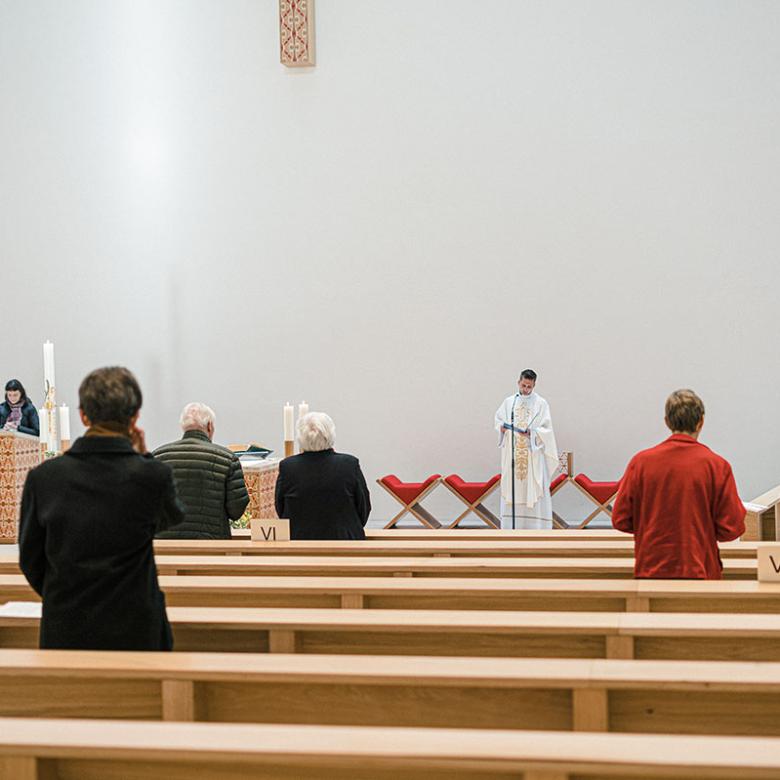 Gottesdienstbesucher stehen nach Anmeldung und mit Abstand zueinander in den Kirchenbänken während einer Messe. Auf den Kirchenbänken platzierte Zettel mit römischen Ziffern markieren mögliche Sitzplätze für Gottesdienstbesucher.