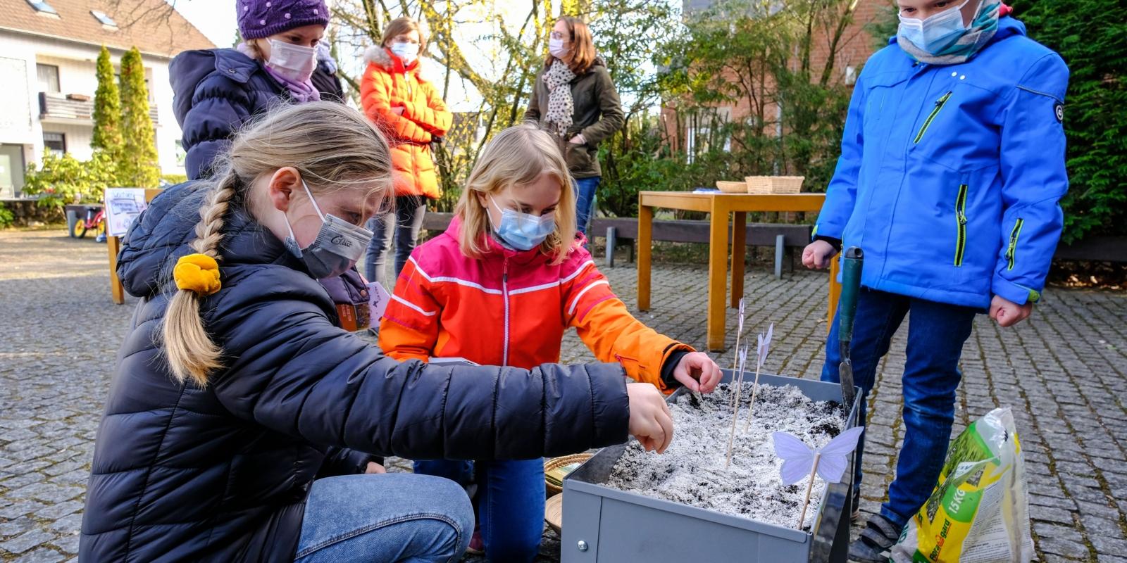 Vanja, Mira, Jonathan und Jana säen vor der Kirche Christus König in Köln-Porz 'Picknickplätze für Schmetterlinge'aus.