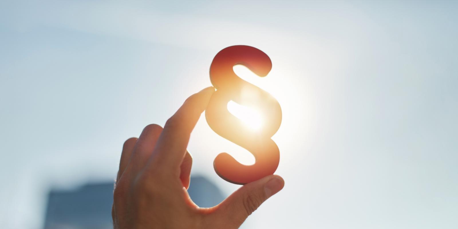 Hand holds paragraph symbol in the sun in the sky