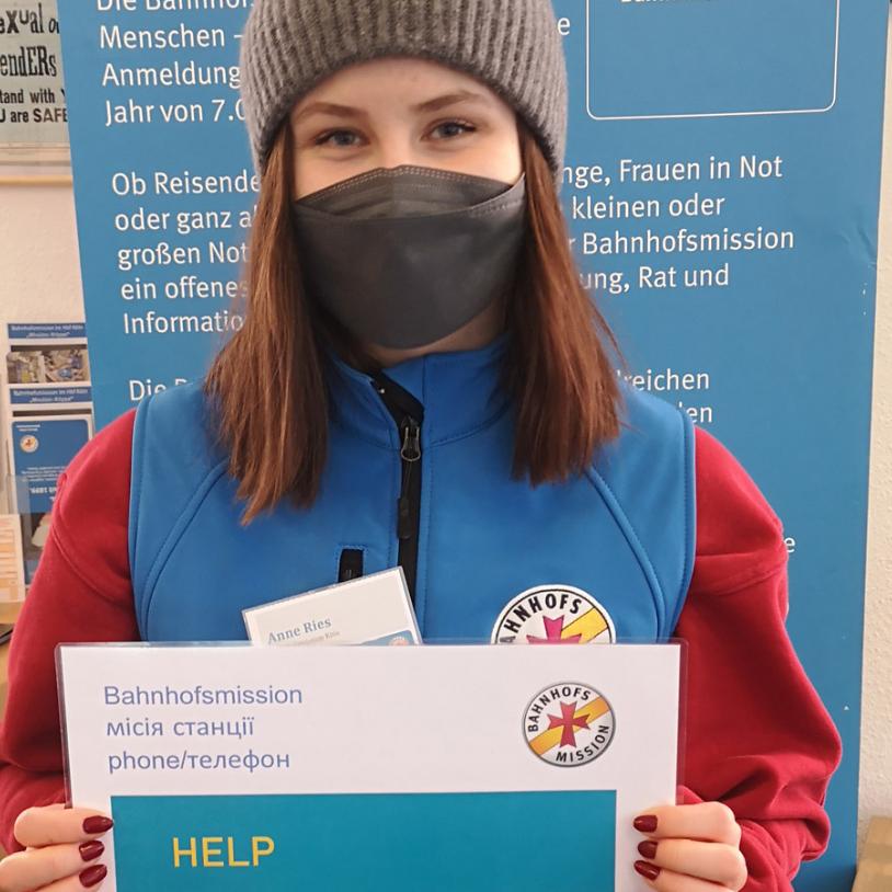Mit einem Schild in Ukrainisch und Englisch beitet eine Mitarbeiterin der Bahnhofsmission Hilfe an.