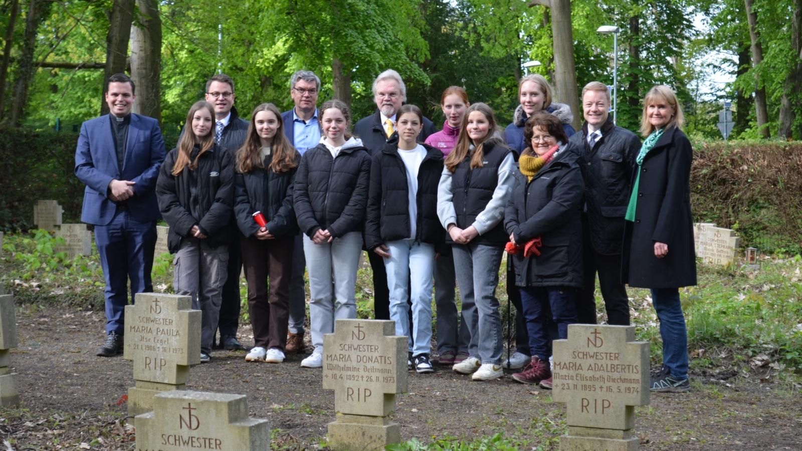 Gruppenbild auf dem Friedhof (v.l.): Daniel Sluminsky (Schulseelsorger), Rafael Bartsch (Erzb. Schulrat), Sophia, Magdalena, Michael Bornemann (Schulleiter), Clara, Norbert Erlinghagen (Vorstand Schulfonds), Olivia, Carlotta, Emma, Josefine, Anna van dem Brink (Religionslehrerin), Thomas Pitsch (Bereichsleiter Schule & Hochschule, Erzbistum Köln), Petra Hennigfeld (stellv. Schulleiterin und Projektbetreuerin).