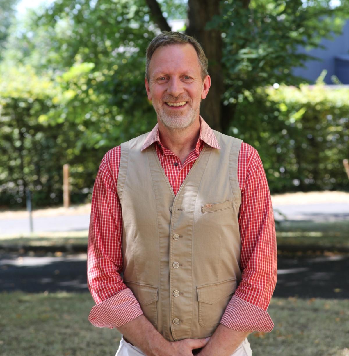 Ein Foto zeigt Schulleiter Christoph Oldeweme mit einem Garten im Hintergrund.