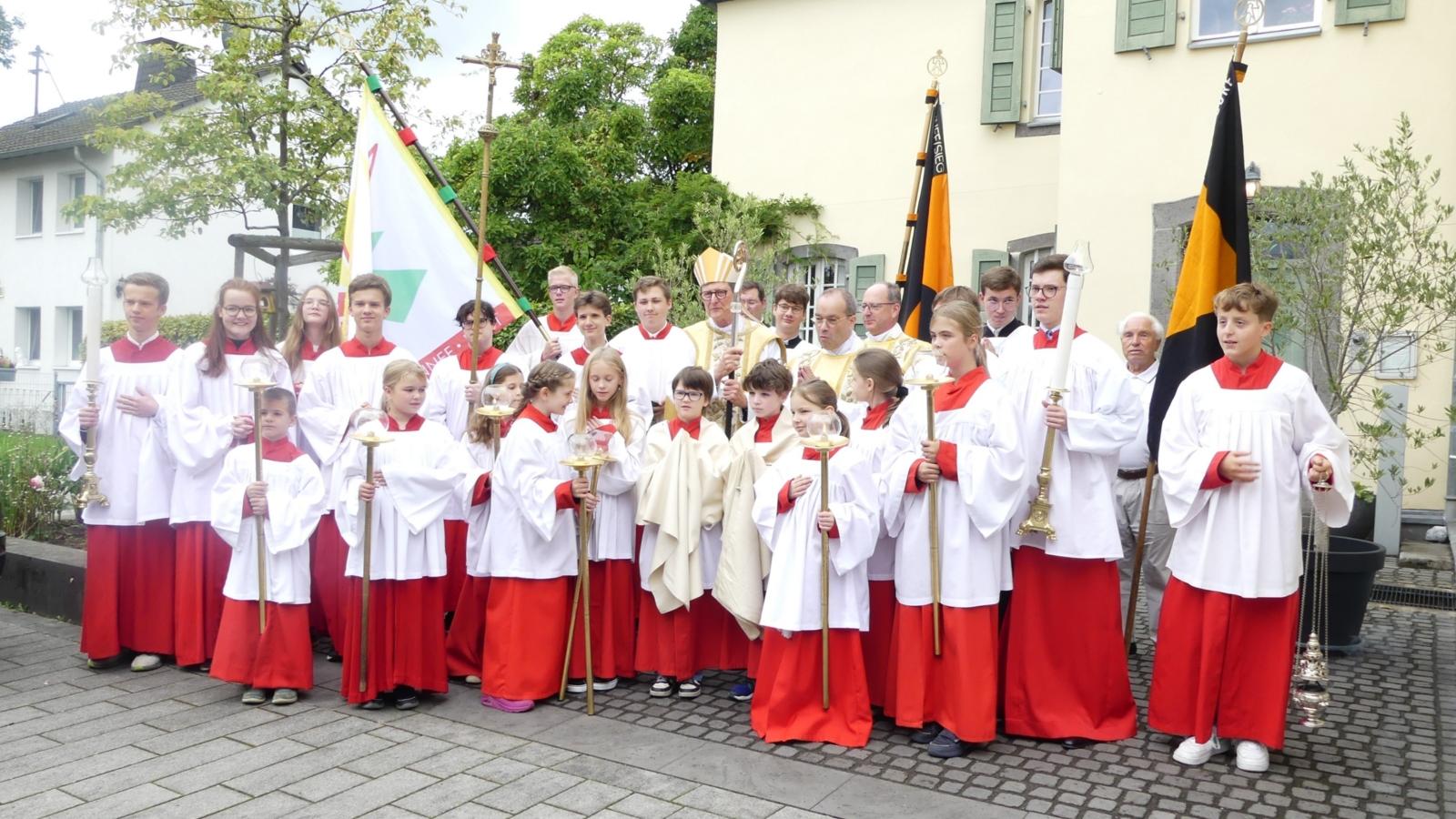 Gruppenbild vor der Pfarrkirche mit Kardinal Woelki, Pfarrer Rick und Pfarrer Lahr sowie zahlreichen Ministranten.