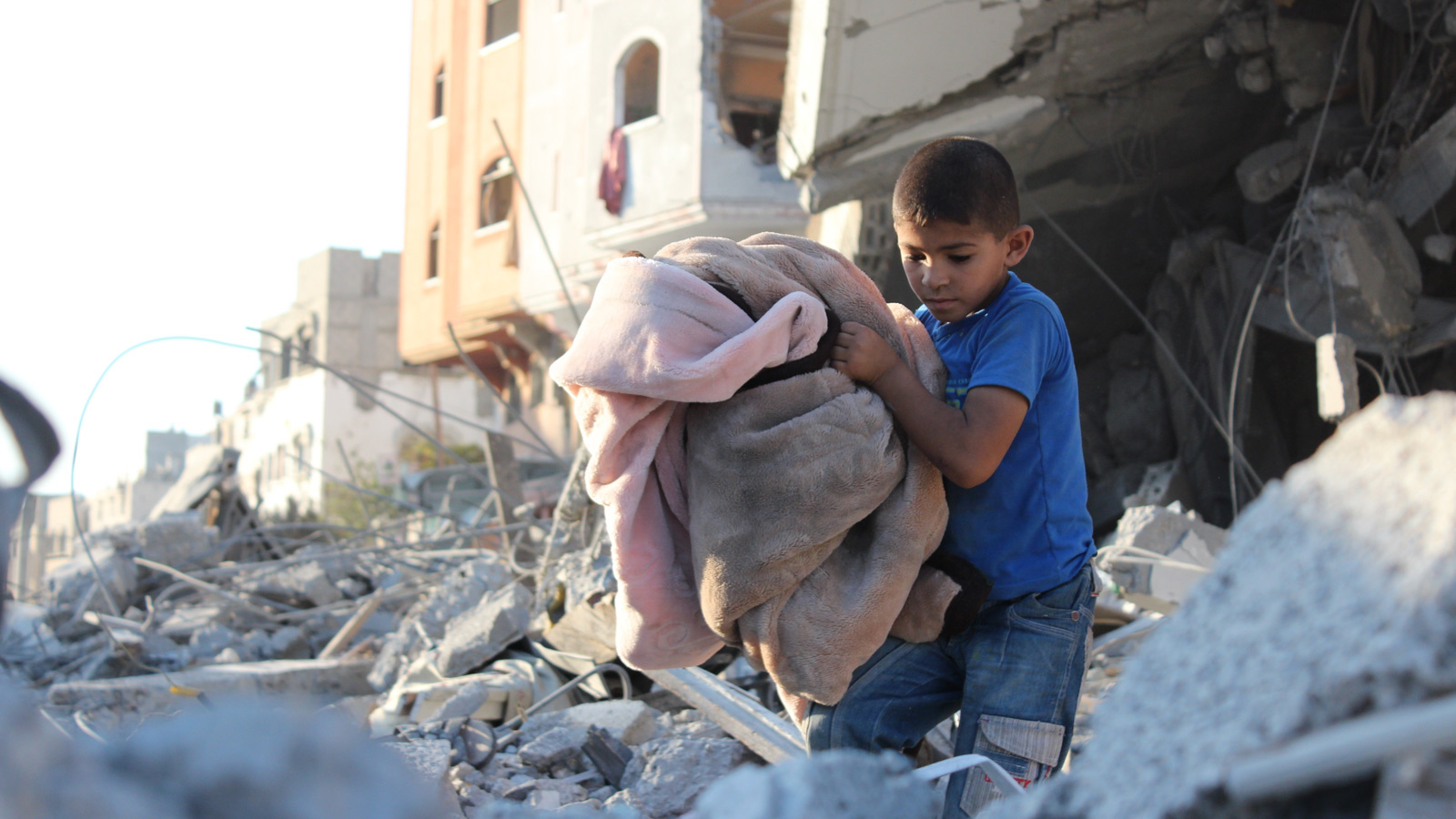 Symbolbild: Junge mit Decken vor zerstörten Häusern im Gaza-Streifen