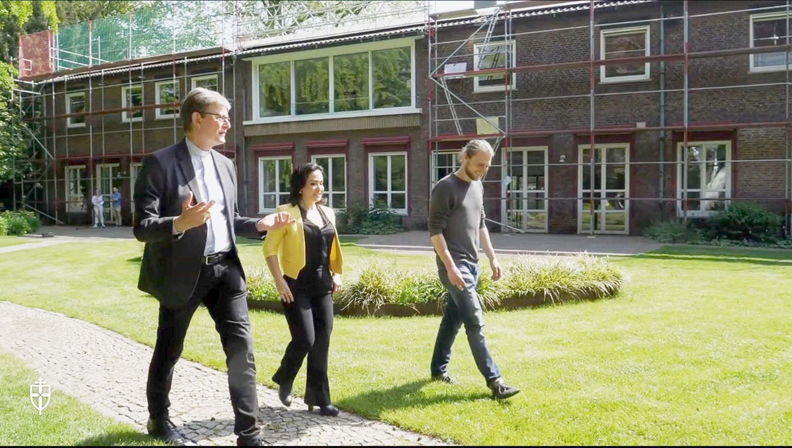 Kardinal Woelki geht mit zwei Erwachsenen durch den Garten des Erzbischöflichen Hauses.