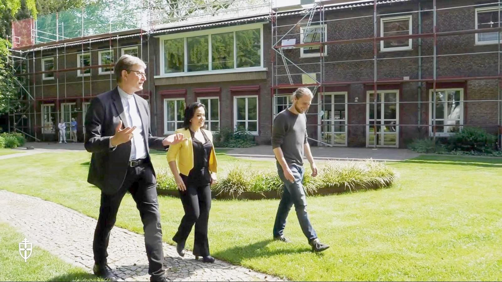 Kardinal Woelki geht mit zwei Erwachsenen durch den Garten des Erzbischöflichen Hauses.