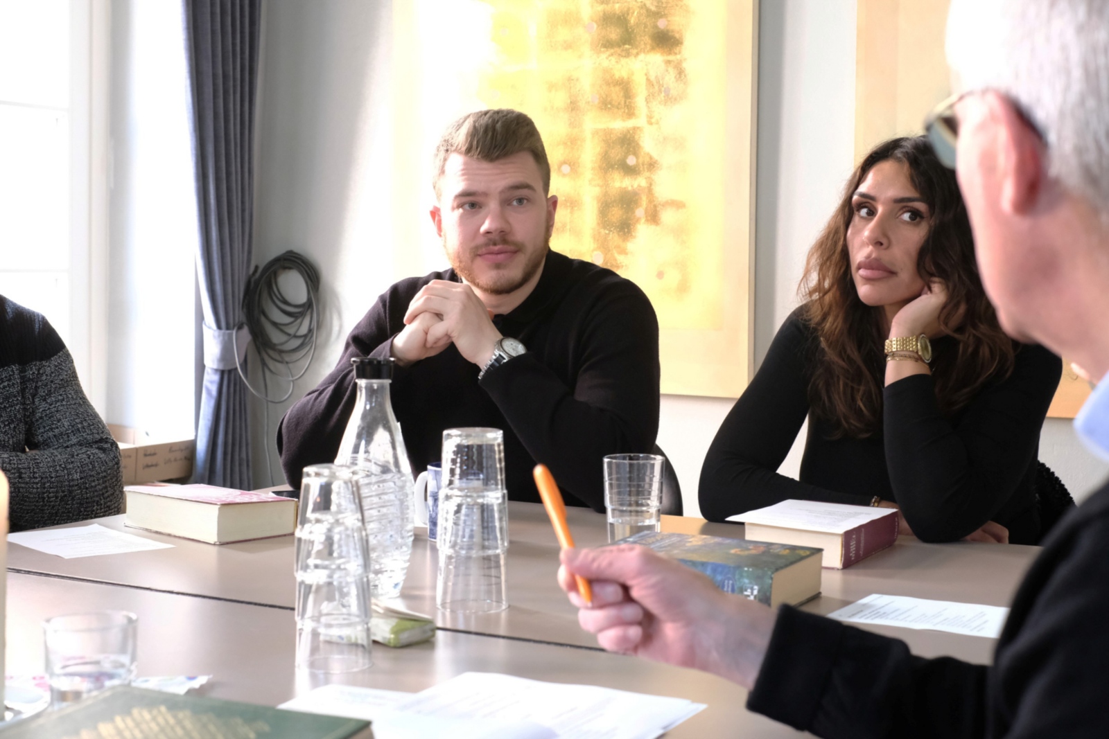 Ein Foto zeigt einen Mann und eine Frau die an einem Tisch sitzen und zuhören.