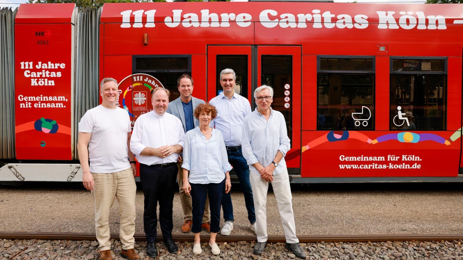 Gruppenbild der Caritas vor einer Straßenbahn der KVB mit Caritas-Kampagnenaufdruck