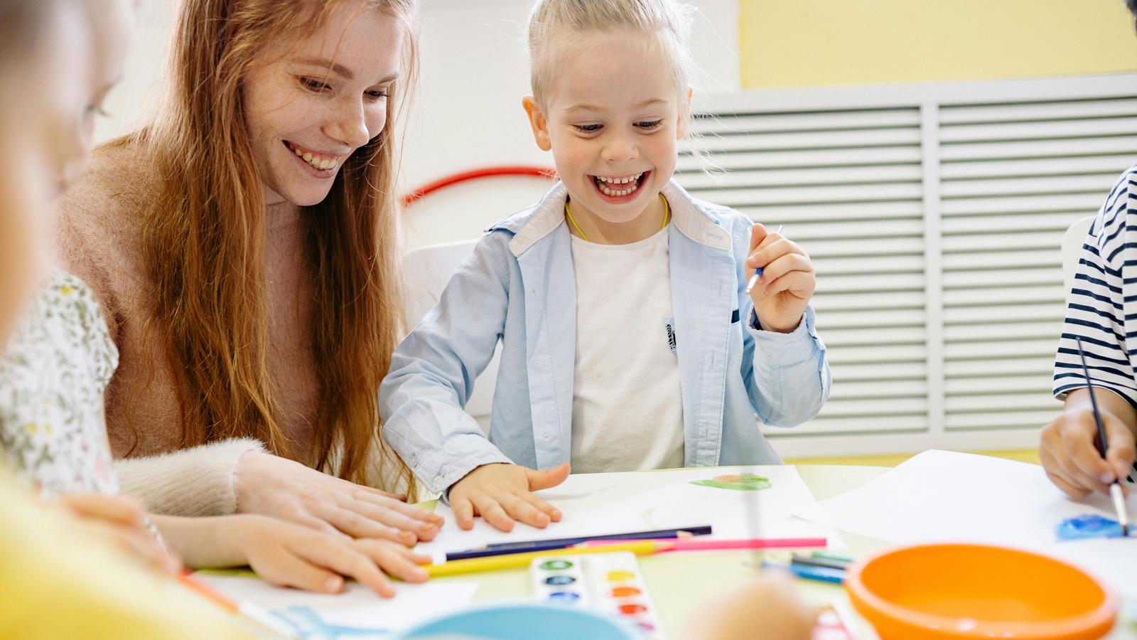 Kunst in der Kita: Kinder malen zusammen mit ihrer Erzieherin Bilder mit Wasserfarben