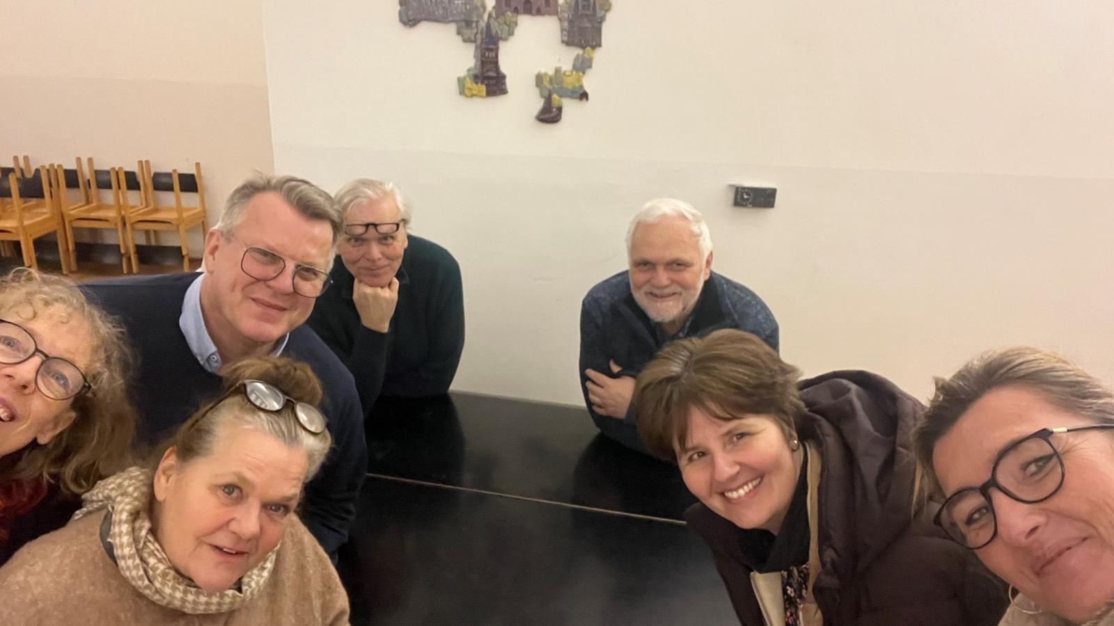 Vier Frauen und drei Männer sitzen um einen Tisch und machen ein Foto von der Gruppe.