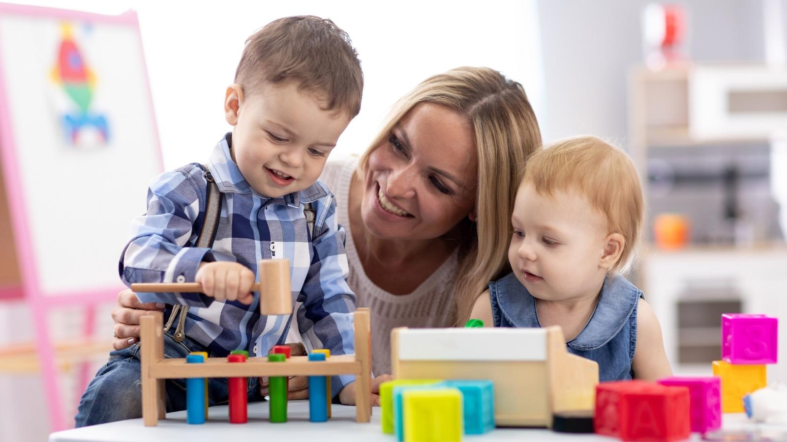 Kinderbetreuerin mit zwei Kleinkindern mit Holzspielzeug am Tisch