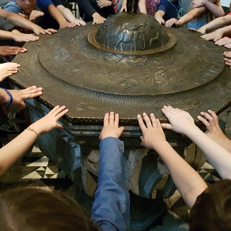 Viele Kinder stehen im Kreis um ein Taufbecken und legen ihre Hand auf den Rand