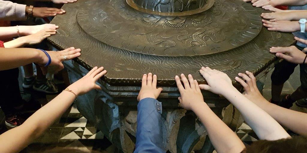 Viele Kinder stehen im Kreis um ein Taufbecken und legen ihre Hand auf den Rand