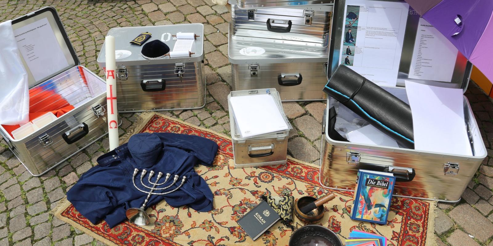 Teppich auf dem diverse Materialien liegen: Osterkerze, Klangschale, Bibel, Koran, etc.