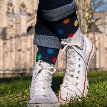 Person, nur sehen sind weiße Sneakern und bunte Socken, steht auf einer Wiese, Kirche im Hintergrund