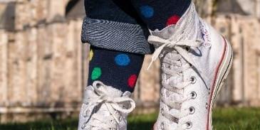 Person, nur sehen sind weiße Sneakern und bunte Socken, steht auf einer Wiese, Kirche im Hintergrund