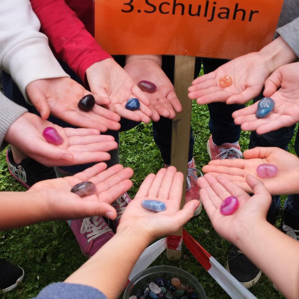 Mehrere Menschen halten einen bunten Stein in ihrer offenen Handfläche und bilden einen Kreis