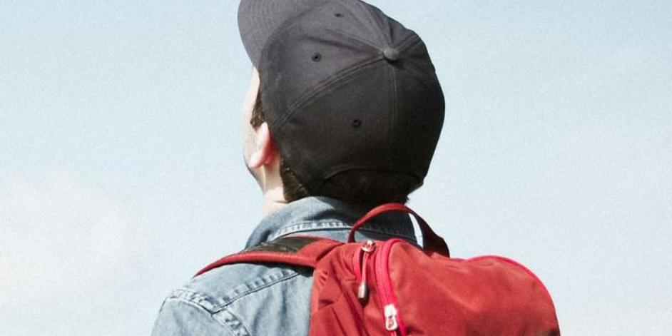 Kind mit Rucksack und Baseballcap schaut in den hellblauen Himmel