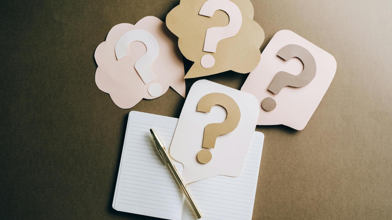 Notizbuch mit Stift und ausgeschnittenen Karten und Fragezeichen aus Tonpapier