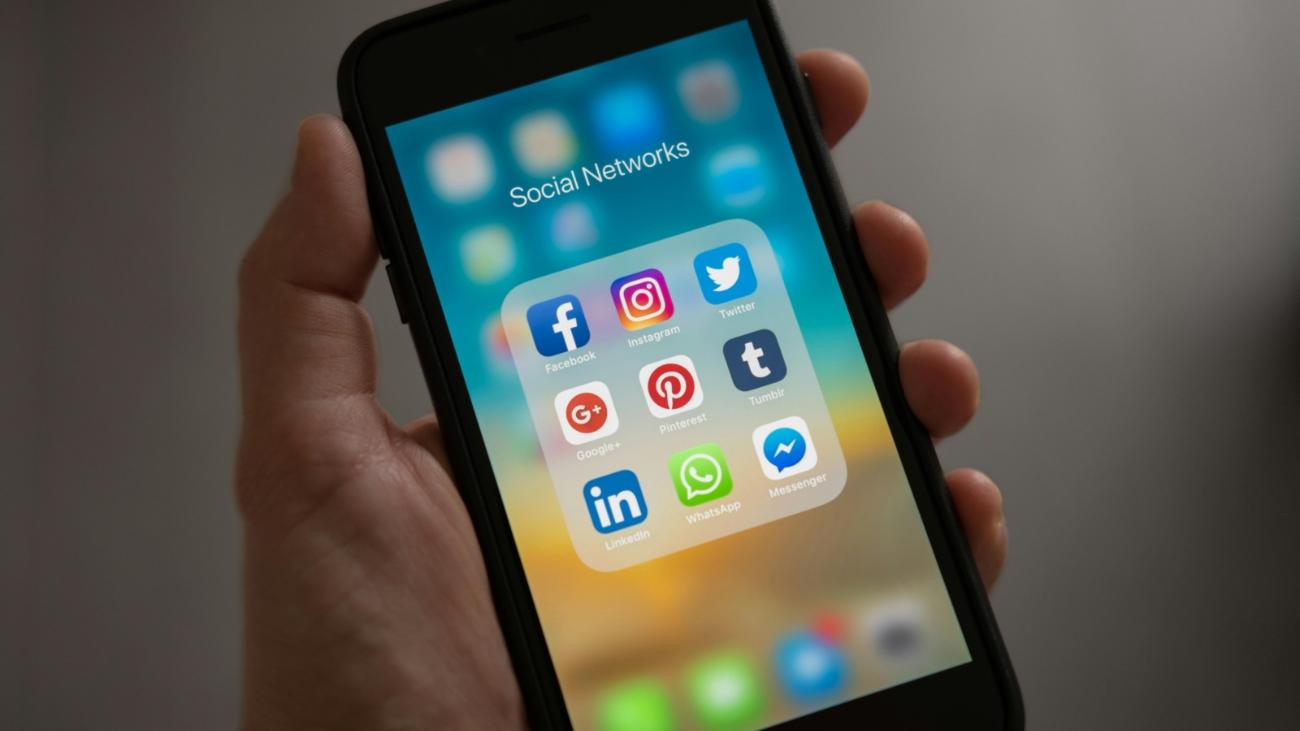Hand hält Smartphone mit Social Media-Buttons im Display