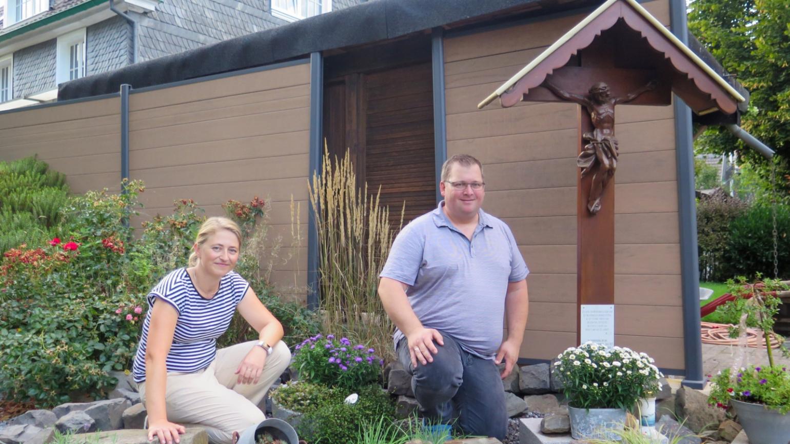 Carmen und Thomas Wülfingan ihrem Flutkreuz in Wuppertal-Beyenburg. Auf der Gedenktafel am Kreuz wird mit Mt 7,25 an die Flutkatastrophe im Juli 2021 erinnert.