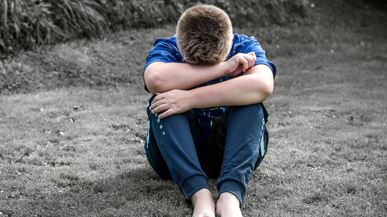 Junger Mensch sitzt mit gesenktem Kopf auf dem Boden