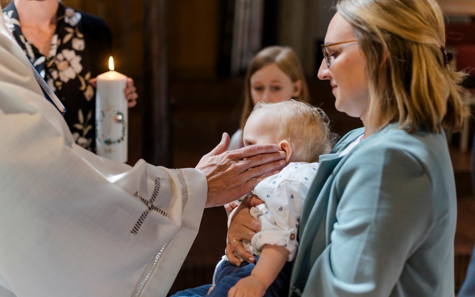 Priester berührt Ohren des getauften Kindes.