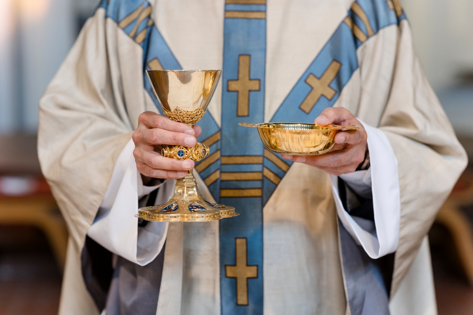 Priester hält Hostienschale und Kelch.