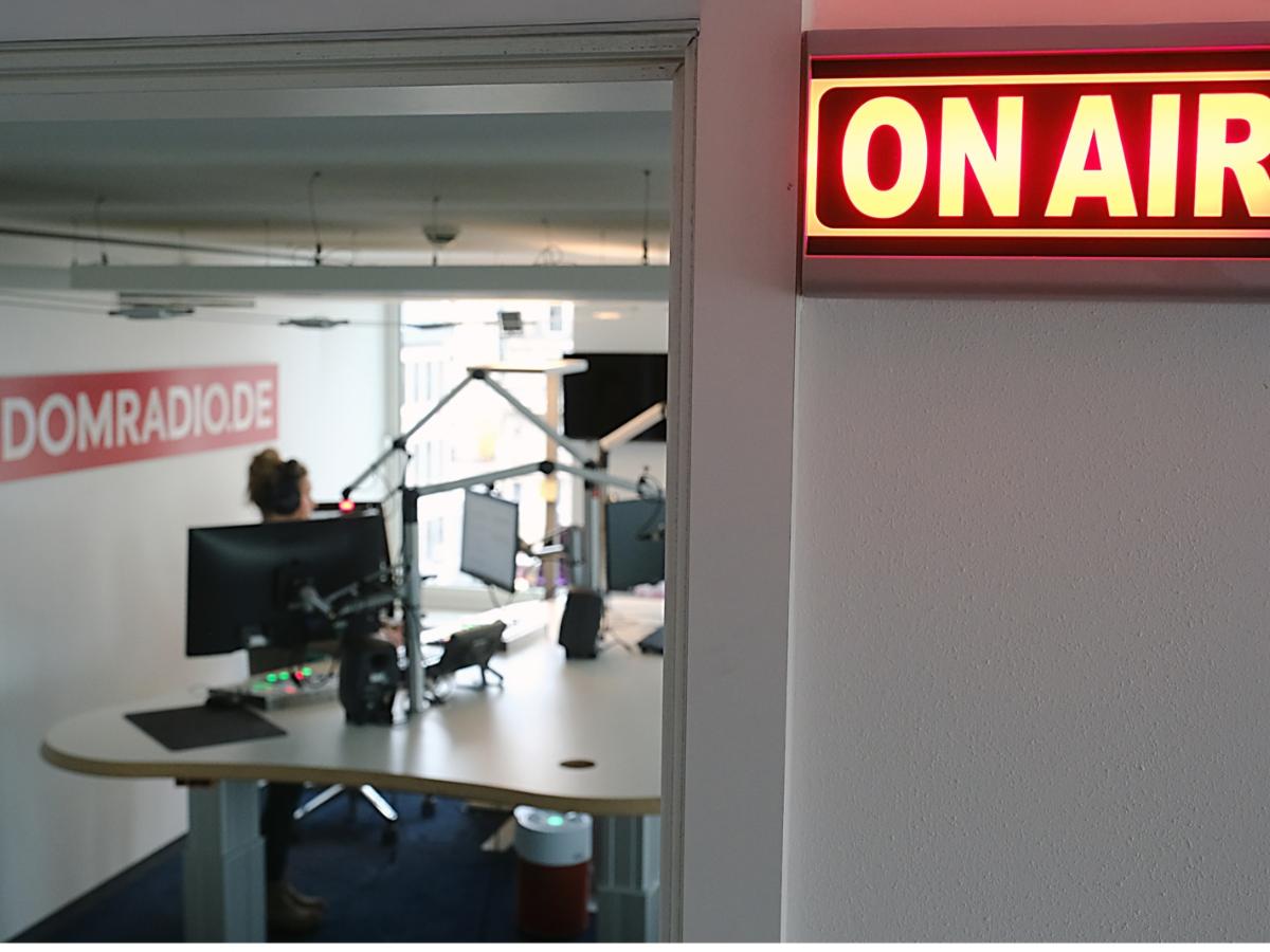 Ein Foto zeigt den Blick in das Radiostudio von Domradio. Vor dem Studio leuchtet ein Schild mit der Aufschrift On Air.