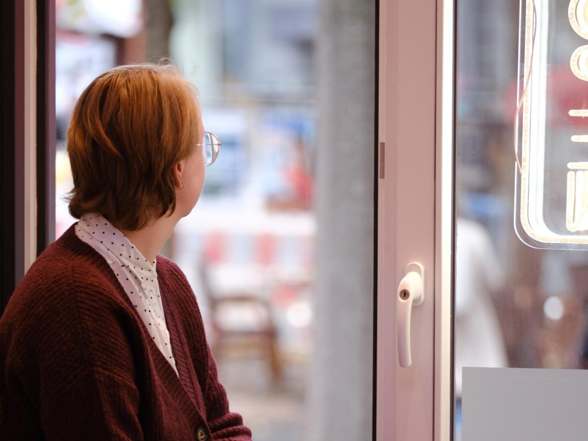 Ein Foto zeigt eine Frau sitzend auf einer Fensterbank, die aus dem Fenster schaut.