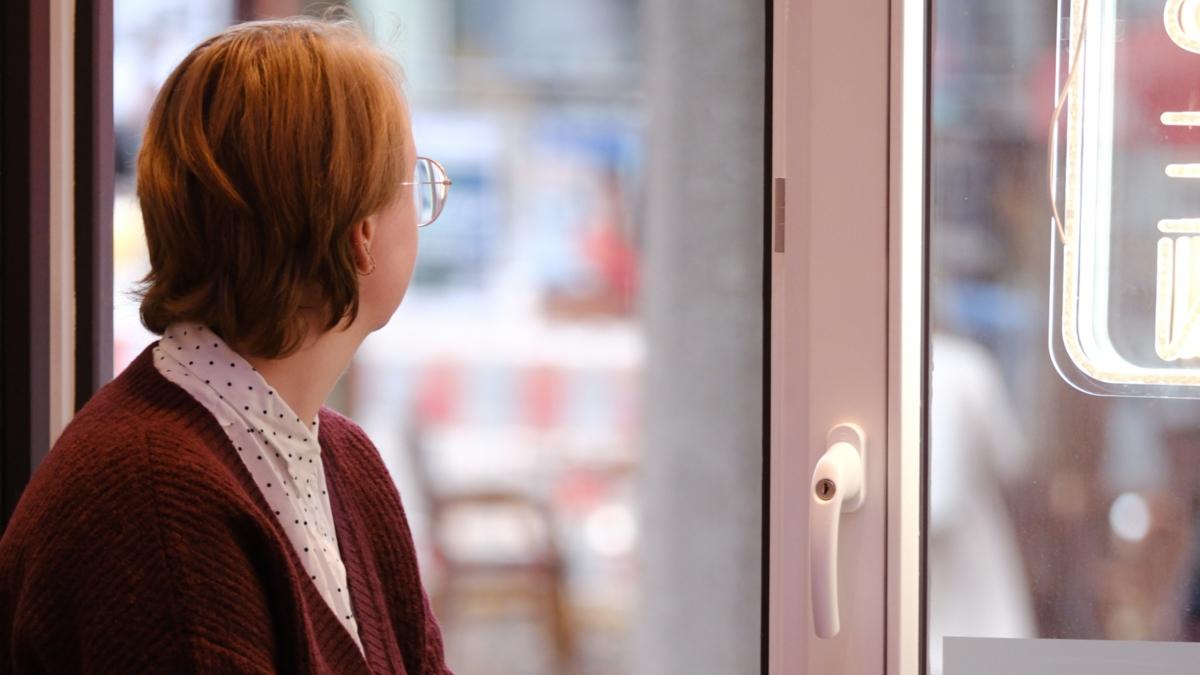 Ein Foto zeigt eine Frau sitzend auf einer Fensterbank, die aus dem Fenster schaut.