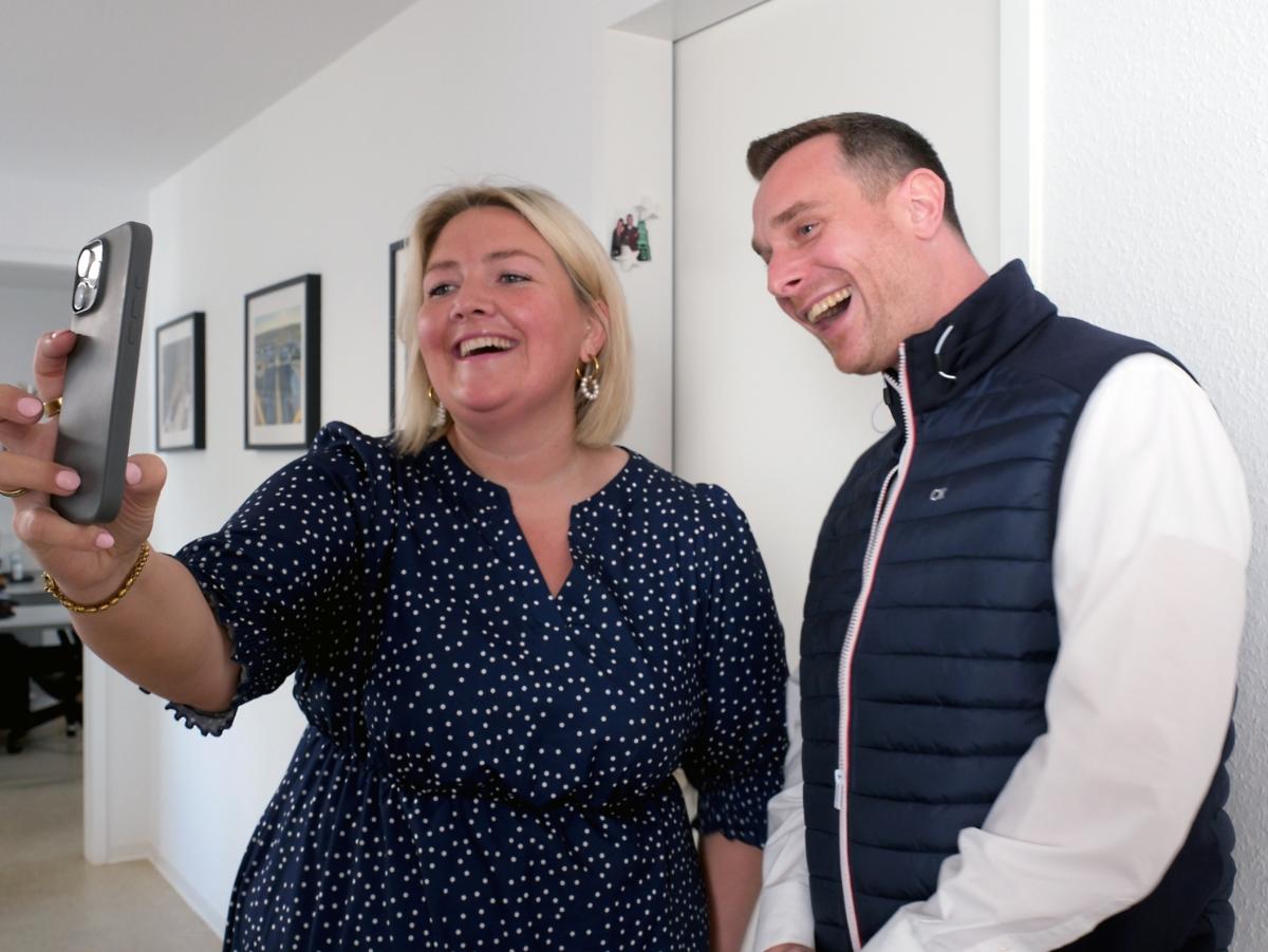 Ein Foto zeigt eine Frau und einen Mann die in eine Handykamera lachen.