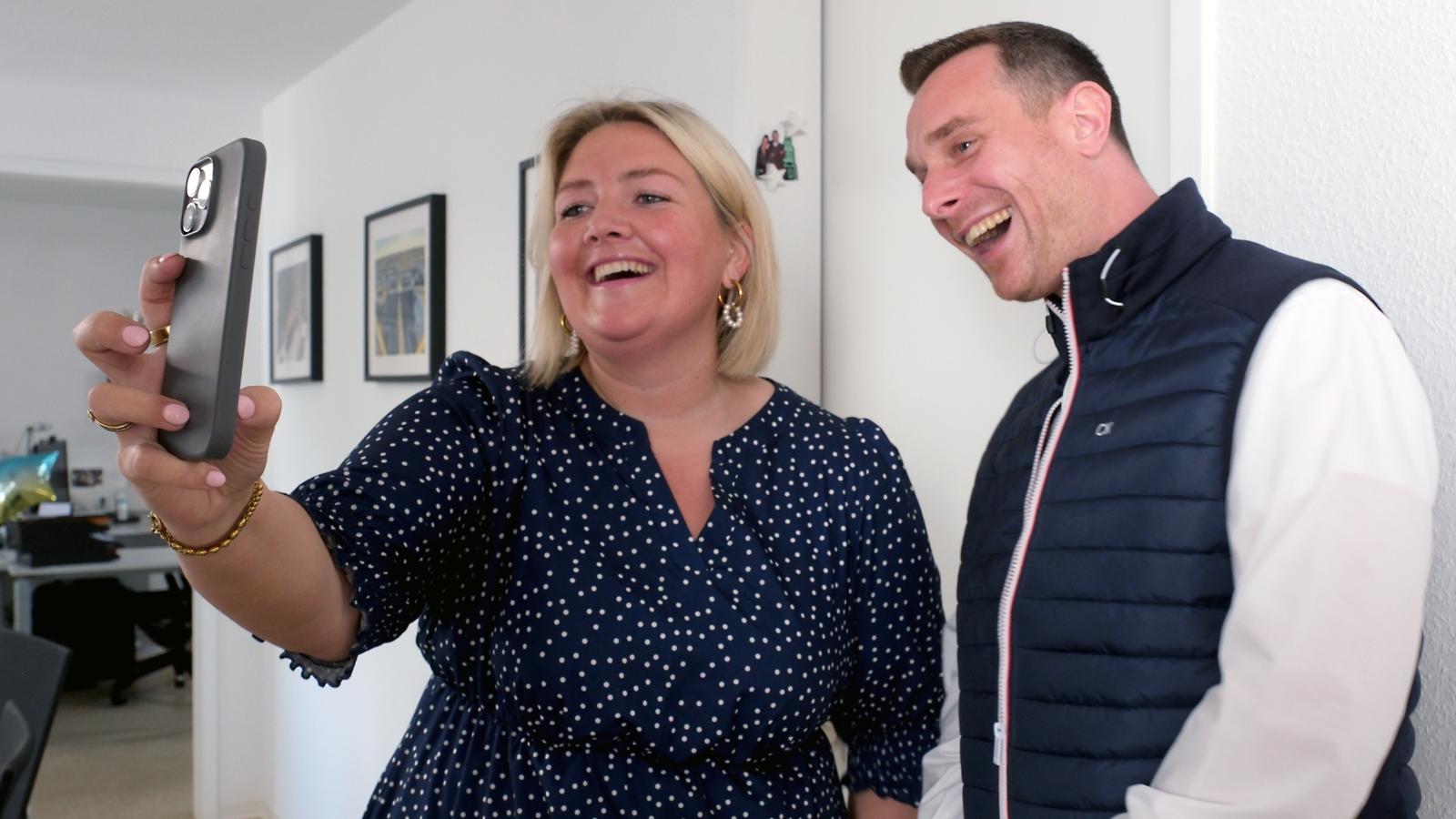 Ein Foto zeigt eine Frau und einen Mann die in eine Handykamera lachen.