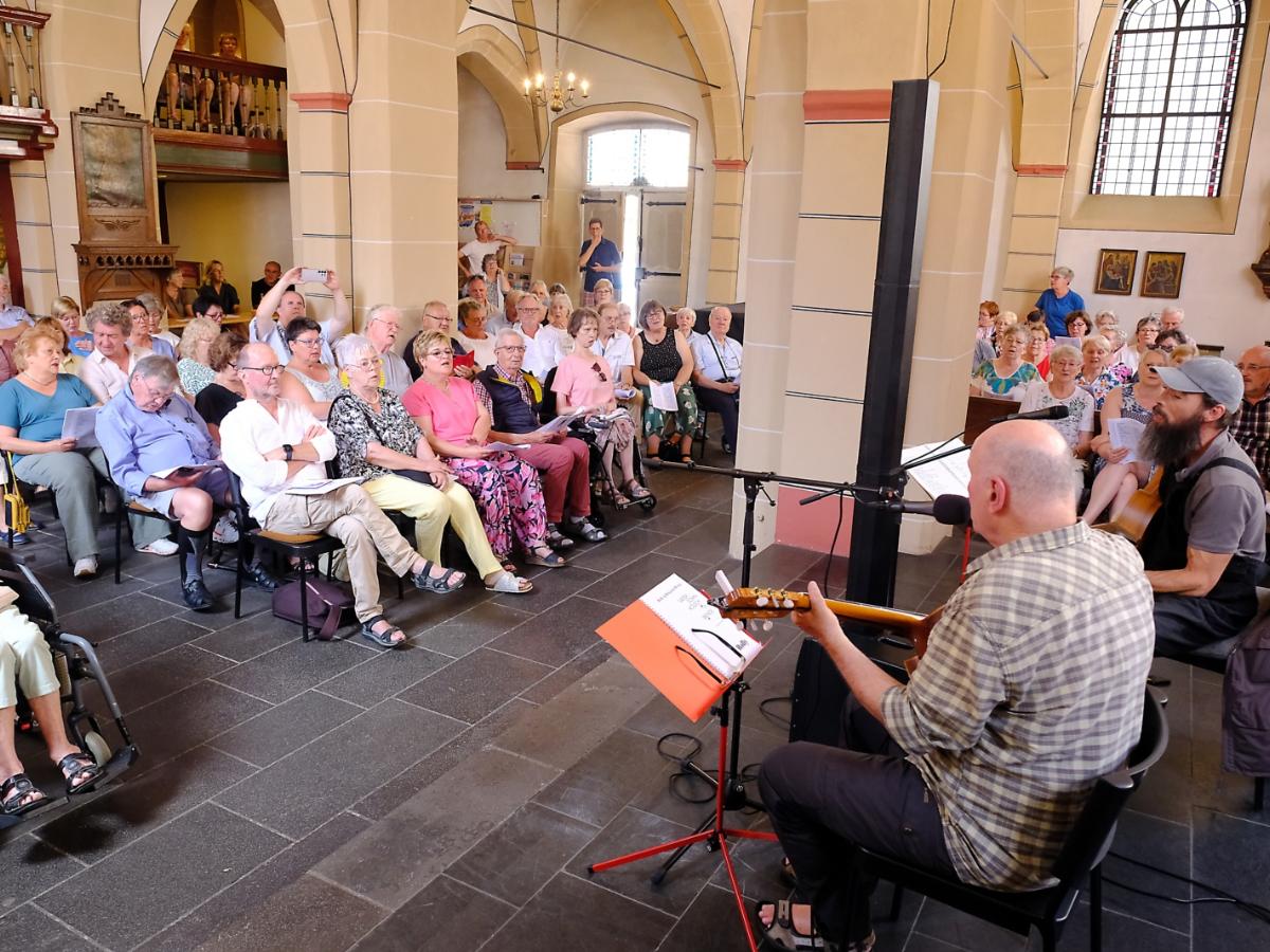 Ein Foto zeigt zwei Männer mit Gitarren vor Publikum in einer Kirche.