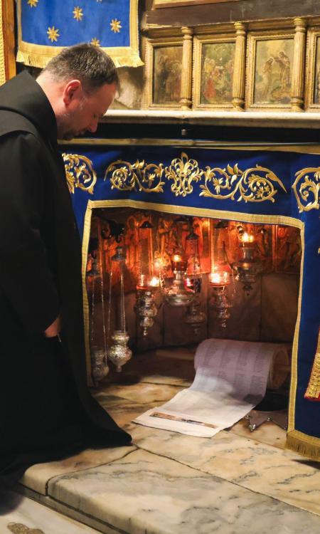 Ein Foto von Abt Nikodemus, der vor einer großen Öffnung in einer Wand kniet, in der die Namensrolle liegt.