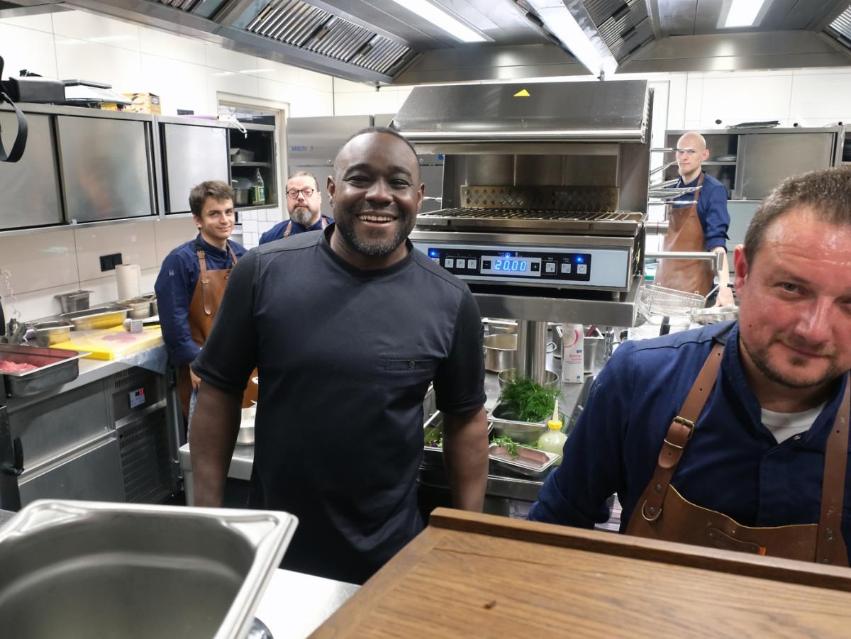 Ein Foto zeigt den Blick in eine Restaurantküche, in der Nelson Müller mit vier Köchen steht.