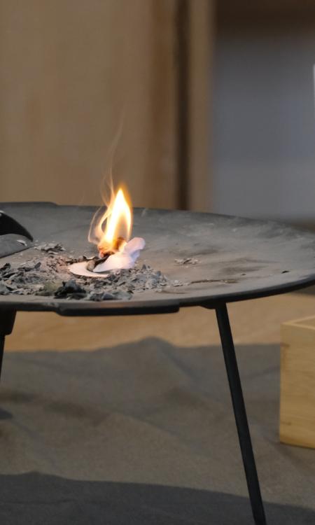 Ein Foto zeigt eine Metallschale auf einem Tisch in der ein kleines Feuer brennt.