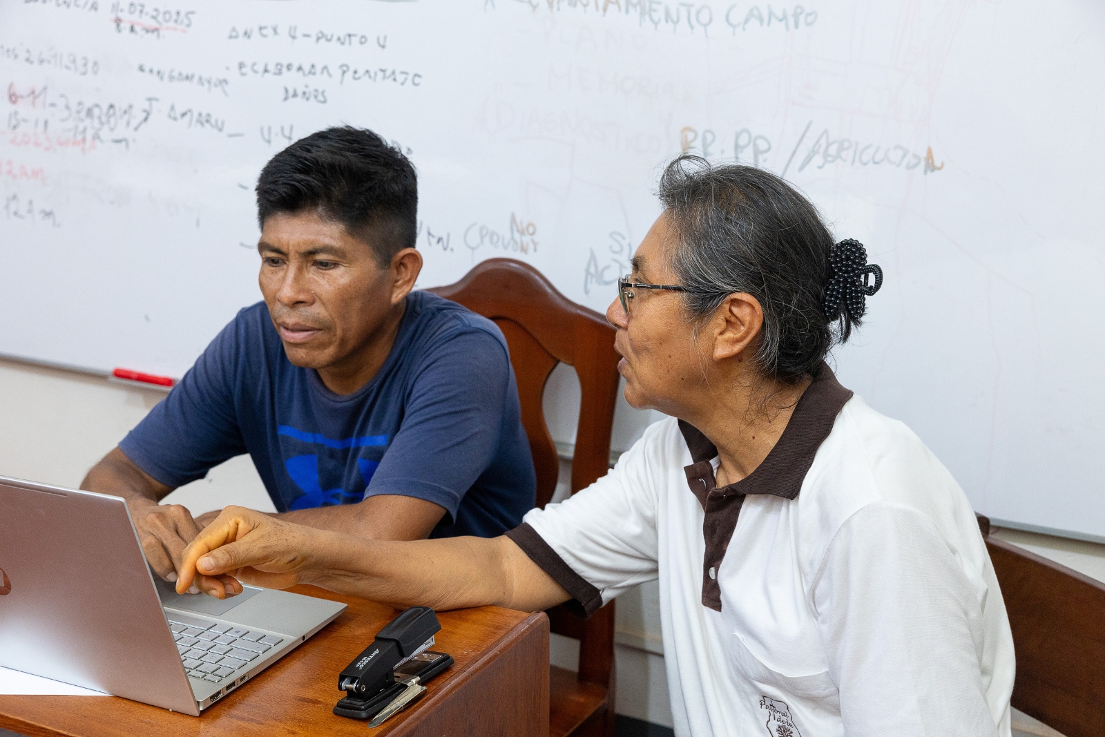 Ein Foto zeigt zwei Personen, die vor einem aufgeklappten Laptop an einem Tisch sitzen.