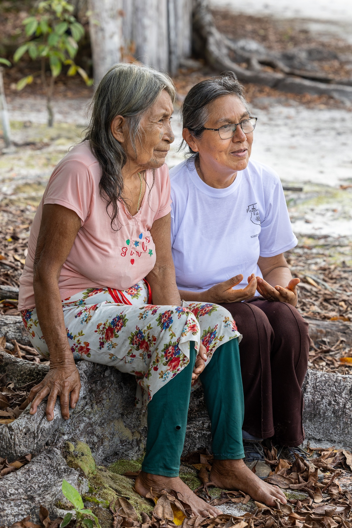 Ein Foto von zwei älteren Frauen, die auf einer Baumwurzel sitzen.