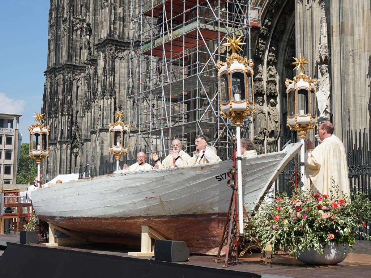 Ein Foto von einem Holzboot vor dem Kölner Dom, das als Altar für einen Gottesdienst genutzt wird.