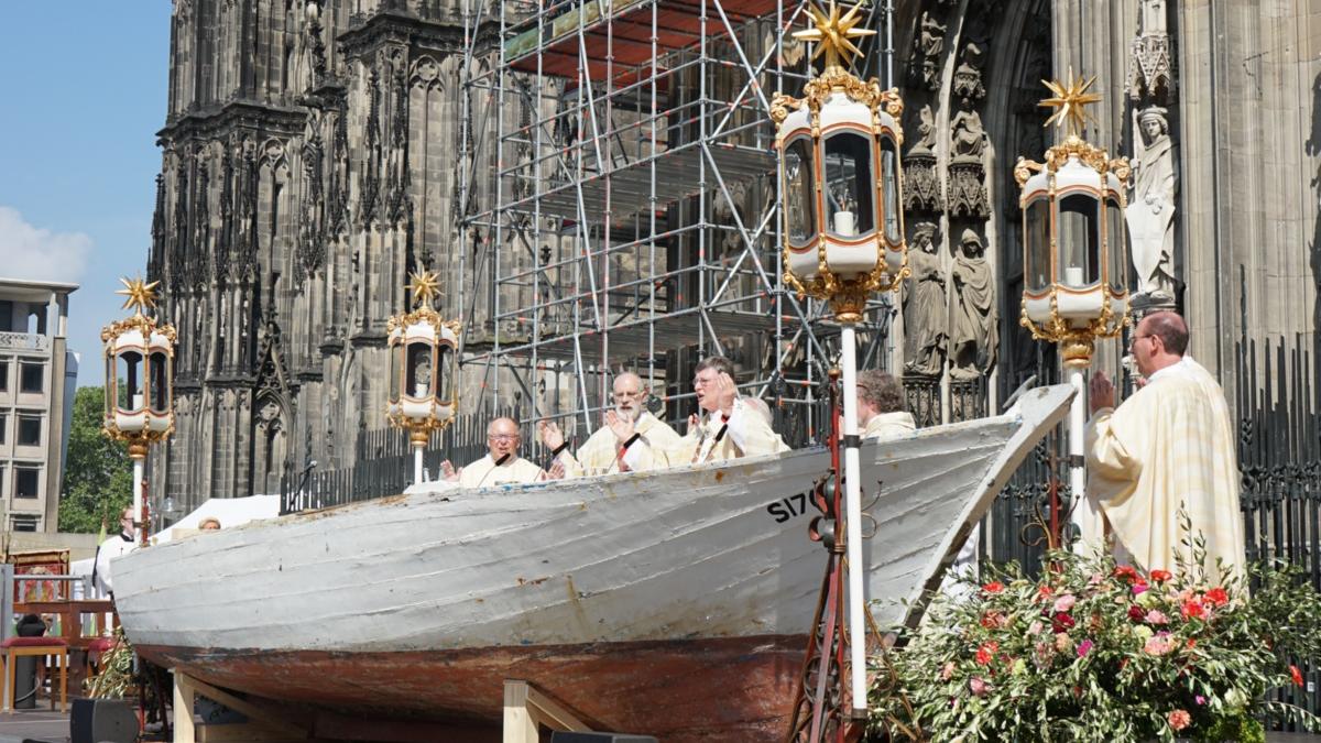 Ein Foto von einem Holzboot vor dem Kölner Dom, das als Altar für einen Gottesdienst genutzt wird.