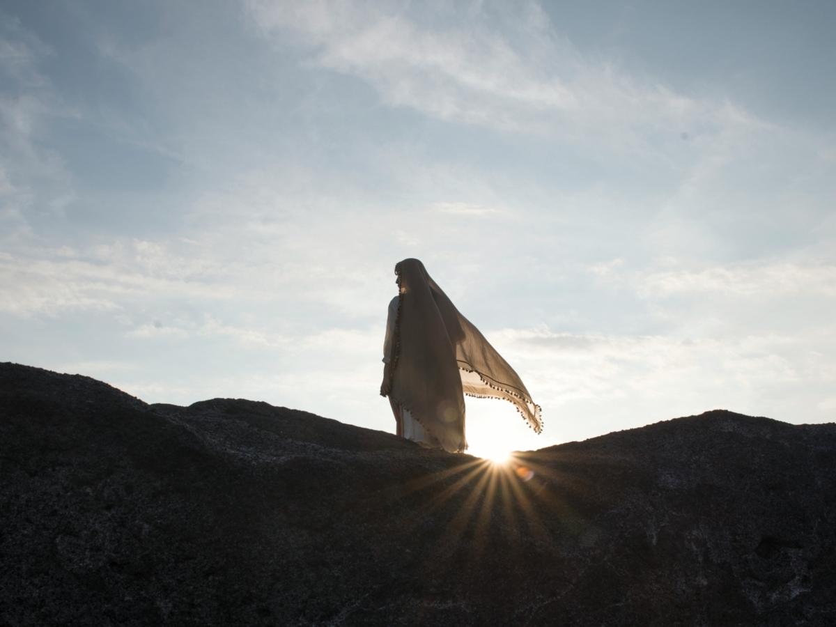 Ein Foto zeigt die Silhouette einer Frau auf einem Felsen im Gegenlicht.