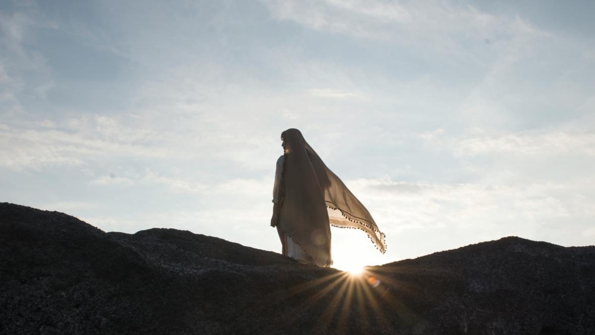 Ein Foto zeigt die Silhouette einer Frau auf einem Felsen im Gegenlicht.