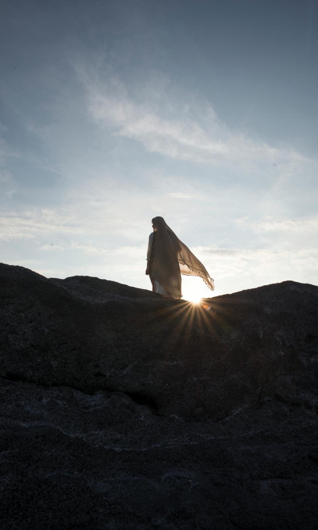 Ein Foto zeigt die Silhouette einer Frau auf einem Felsen im Gegenlicht.